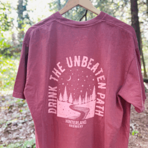 Red shirt hanging in the woods, on the back it says drink the unbeaten path, Hinterland Brewery.
